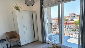 Ett rum med en säng, en stol, en garderob och utsikt över en balkong med byggnader.