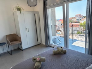 A room with a bed, a chair, a wardrobe, and a view of a balcony with buildings. - Summer holiday apartment- spacious sea view terrace- 2 min walk to the beach (Brodarica)