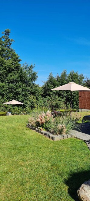 A well-maintained garden with two umbrellas, a brick wall, and a variety of plants.