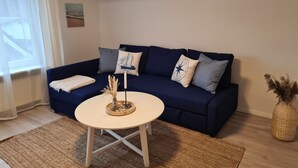 Un salon avec un canapé bleu foncé, une table basse ronde blanche et un tapis tissé.