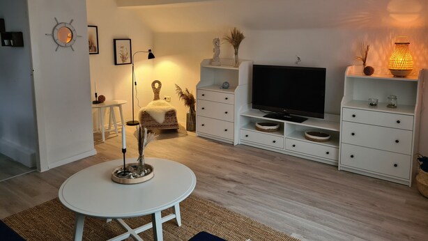 Un salon moderne avec une table ronde blanche, un téléviseur à écran plat et un meuble blanc avec des tiroirs.