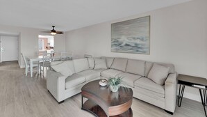 A modern living room with a sectional sofa, a dining table with chairs, a coffee table with a plant, and a ceiling fan. - BEACHFRONT ON A BUDGET!  MILLION $ VIEW!  2B/2B ISLAND VACATION CONDO! (Fort Myers Beach)