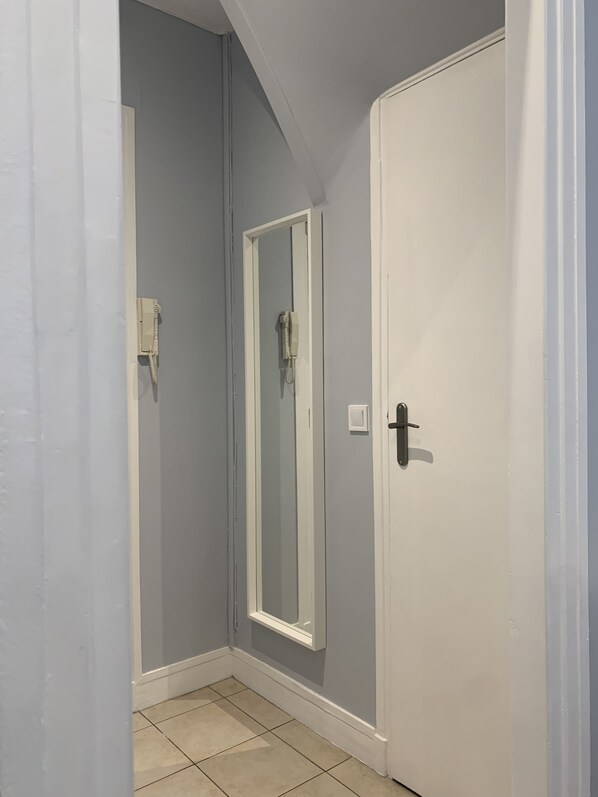 Een smalle gang met een witte deur, een spiegel met een witte lijst en een telefoon aan de muur.