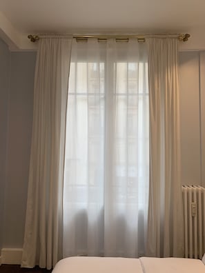 Un dormitorio con una cama, un radiador y cortinas translúcidas.