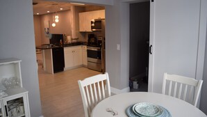 A modern kitchen with white cabinets, a dining table with chairs, and a sliding door leading to another room.