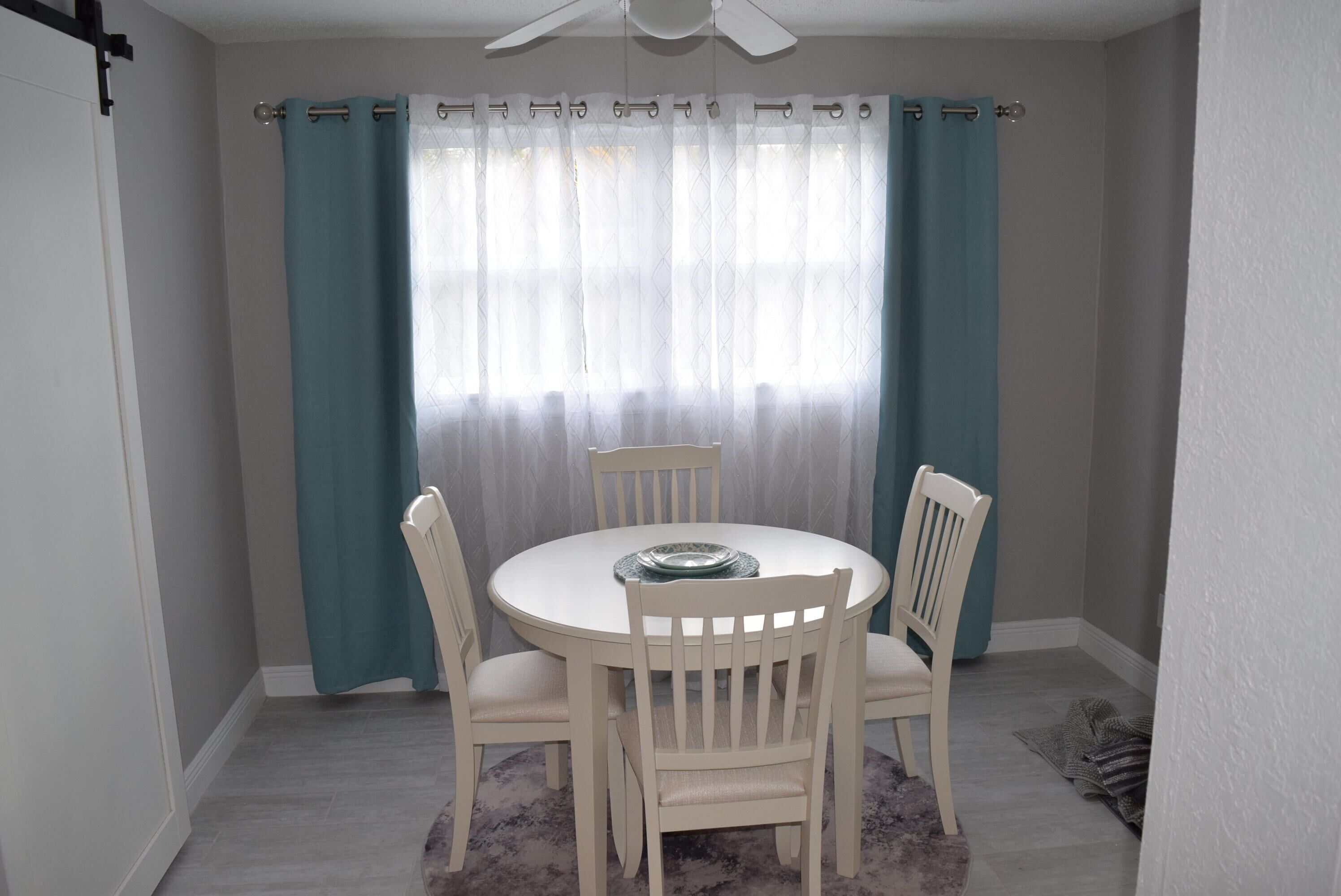 Uma área de jantar com uma mesa redonda, quatro cadeiras e um ventilador de teto.