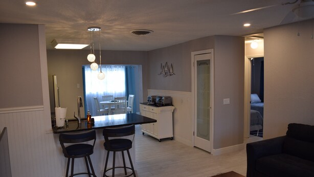 A modern kitchen with a central island, bar stools, and a dining area with a blue curtain.