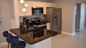 A modern kitchen with white cabinets, a stainless steel refrigerator, a microwave, and a bar area with stools.