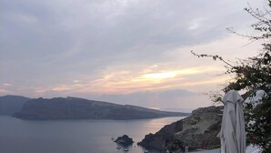 A coastal view with white buildings, a body of water, and a sunset. - Oia Memories Suites (Santorini)