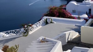 A coastal view with white buildings, a clear blue sea, and rocky cliffs. - Oia Memories Suites (Santorini)