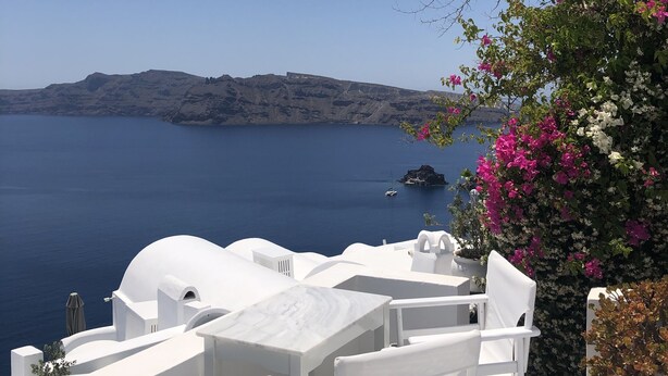 A white outdoor seating area with a view of the sea and a distant island. - Oia Memories Suites (Santorini)