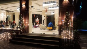 Fachada de hotel de vidrio, adornos navideños y una persona sentada en el interior.