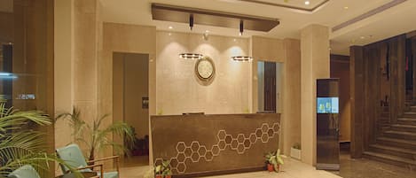A lobby with a reception desk, a large chandelier, and a staircase.