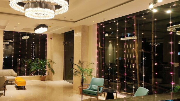 Un moderno vestíbulo con un sofá, sillas y una mesa de centro. Hay plantas en macetas y un gran ventanal con luces decorativas.