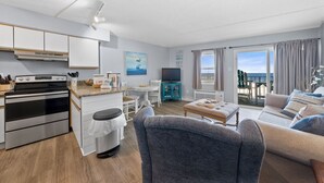 Une cuisine moderne équipée d’une cuisinière, un coin repas avec une table et des chaises, un salon avec un canapé et un téléviseur, et un balcon avec vue.