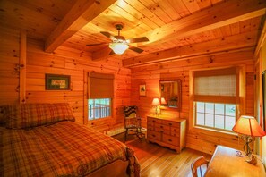 Ein gemütliches Cabin-Zimmer mit Bett, Kommode, Stuhl und Deckenventilator.