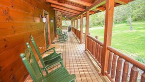 A wooden porch with green rocking chairs and a stone wall.