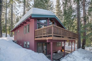 A cabin with a red exterior, a balcony, and a snow-covered roof.