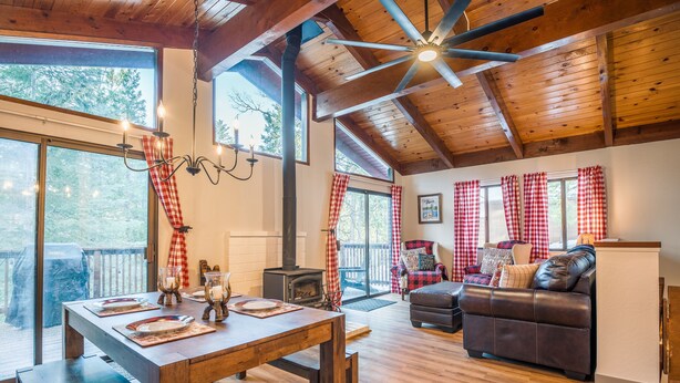 A spacious living area with a wooden ceiling, a fireplace, a dining table set with plates, and a leather sofa. - Sugar Pine Retreat - A/C & Pool Access (Camp Connell)