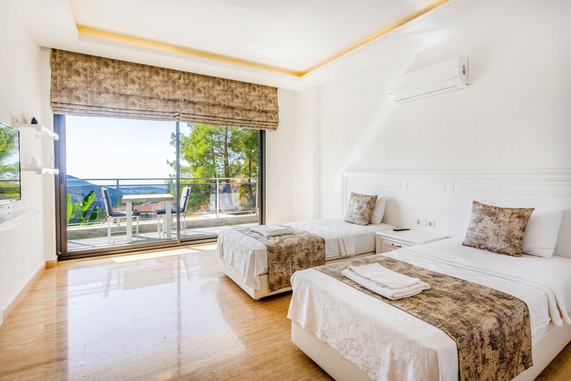 A hotel room with two beds, a large window with a view, and a balcony.
