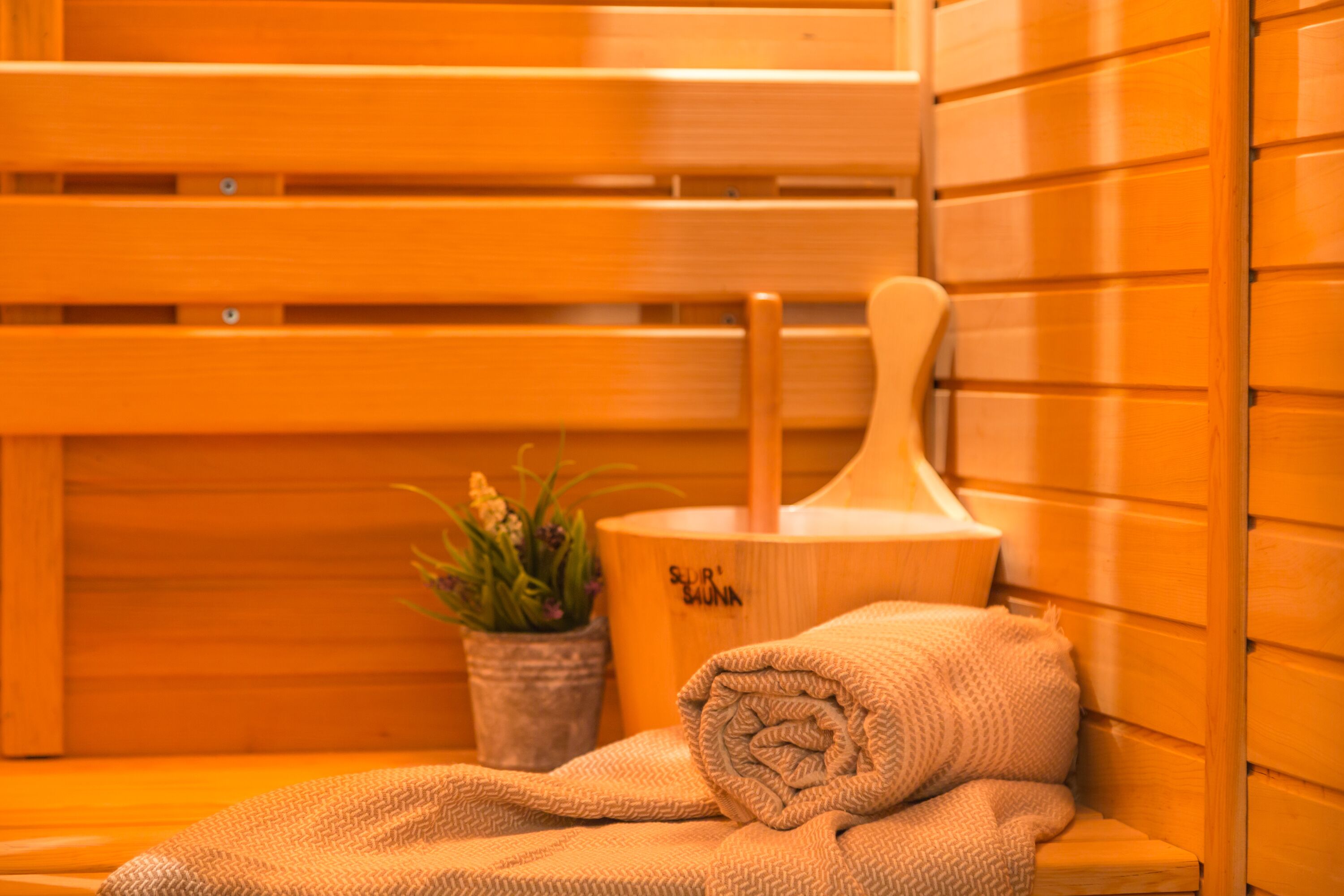 A wooden sauna bench with a towel and a wooden bucket.