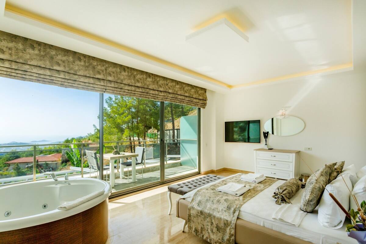 Un dormitorio con un ventanal grande, una bañera y un balcón con mobiliario exterior.