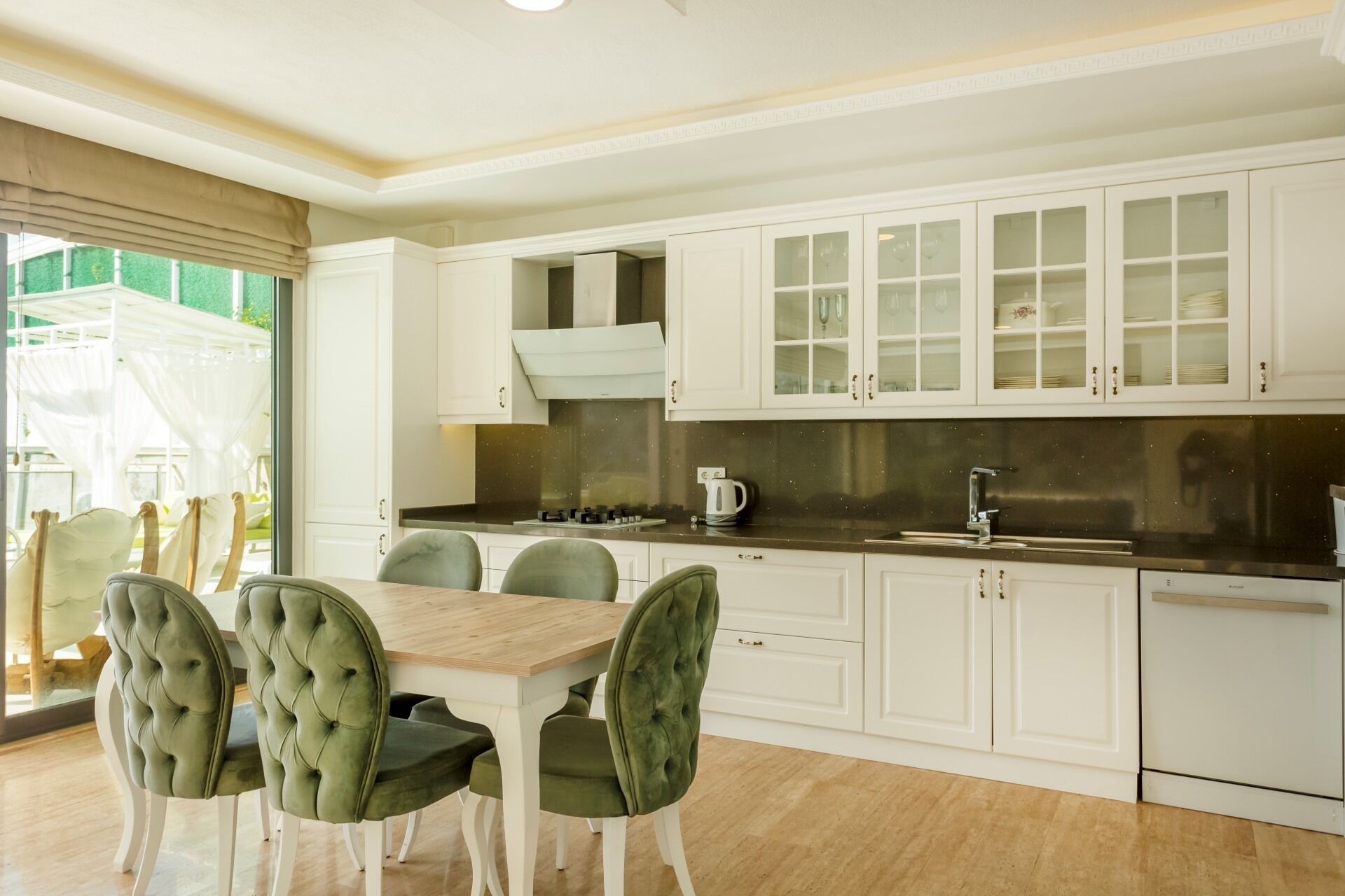 A modern kitchen with white cabinets, a wooden dining table, and green upholstered chairs.