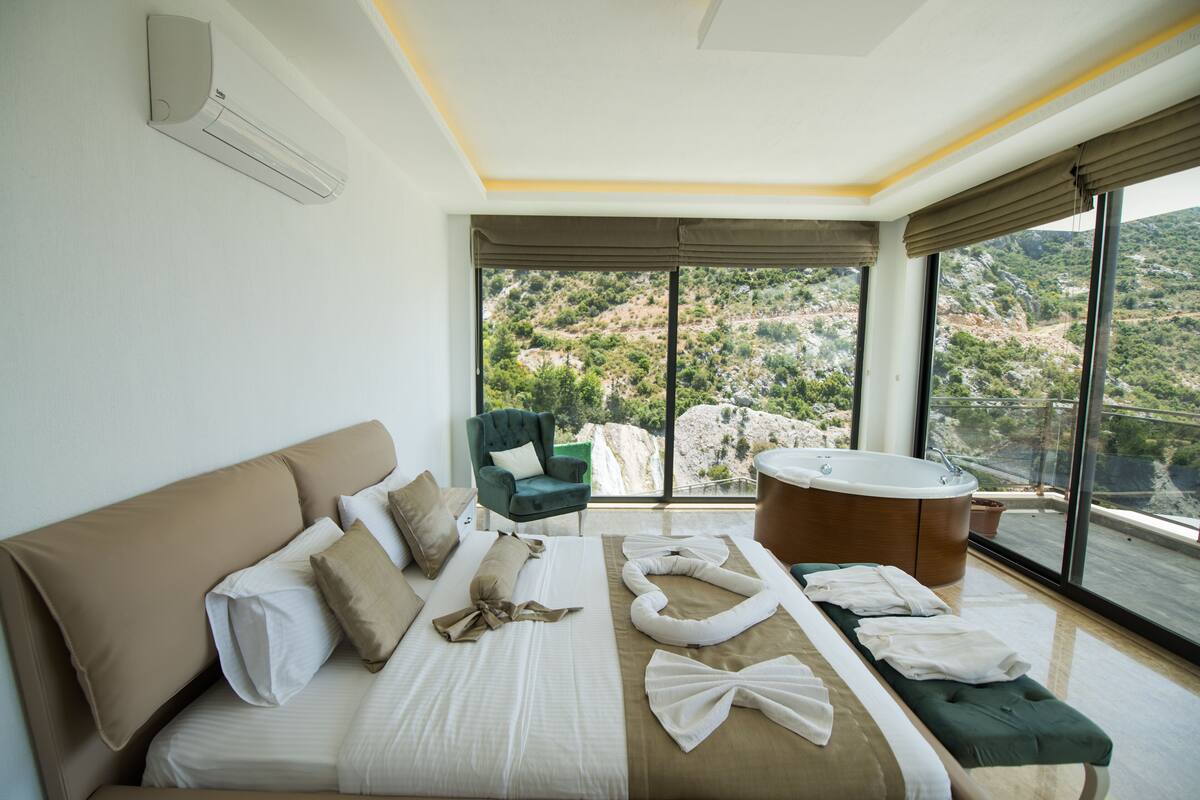 Un dormitorio moderno con una cama grande, un sillón verde, una bañera y vistas a un paisaje montañoso.