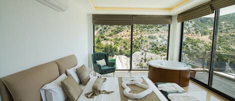 Un dormitorio moderno con una cama grande, un sillón verde, una bañera y vistas a un paisaje montañoso.
