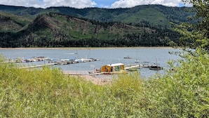 Une vue sur le lac, avec des bateaux amarrés, un petit bâtiment et des collines boisées en arrière-plan.