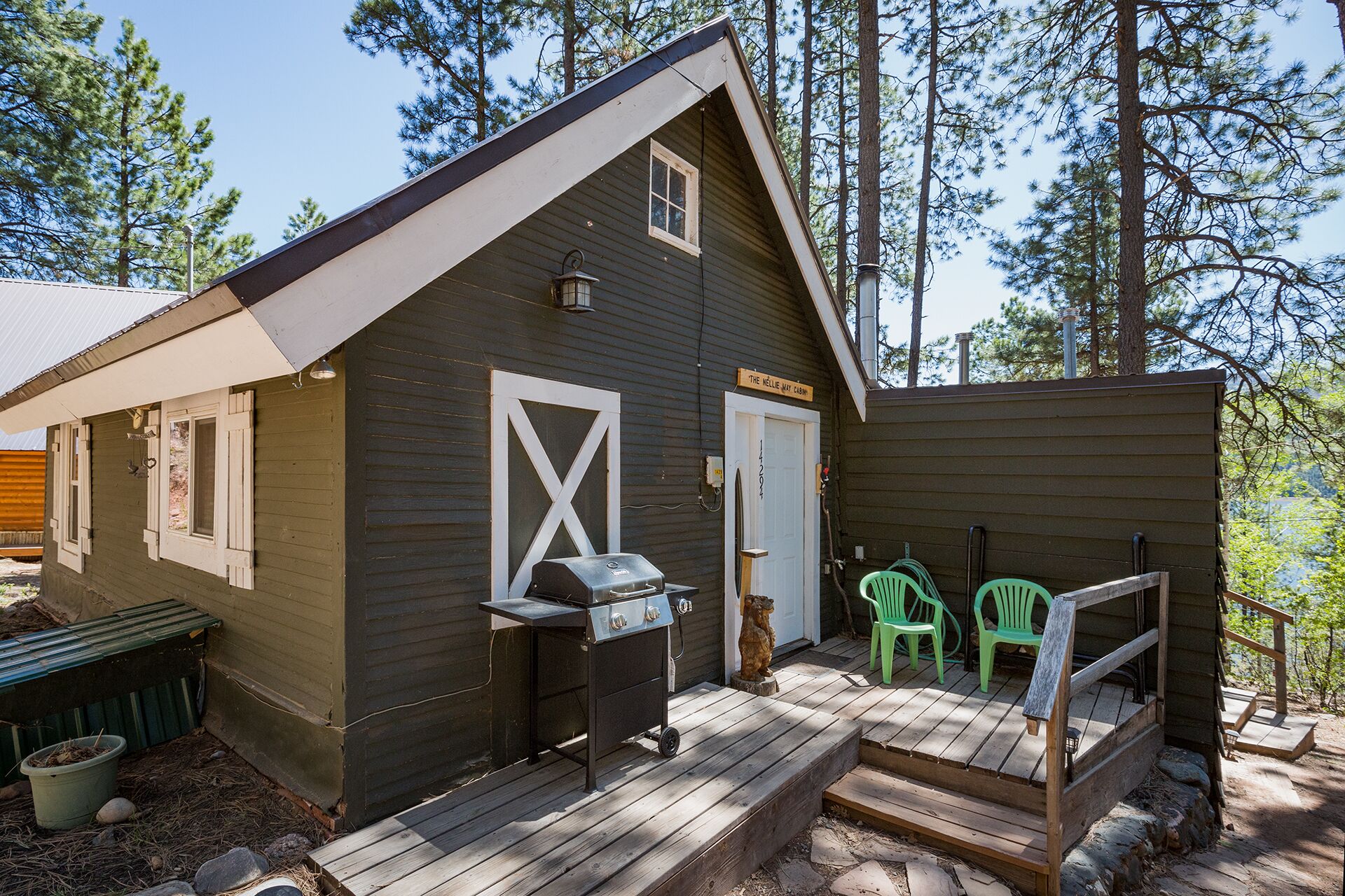 A wooden cabin with a porch, a grill, and two green chairs.