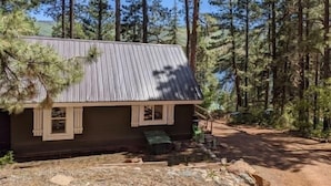 Une cabane avec un toit en métal, des volets en bois et un chemin de terre qui y mène.