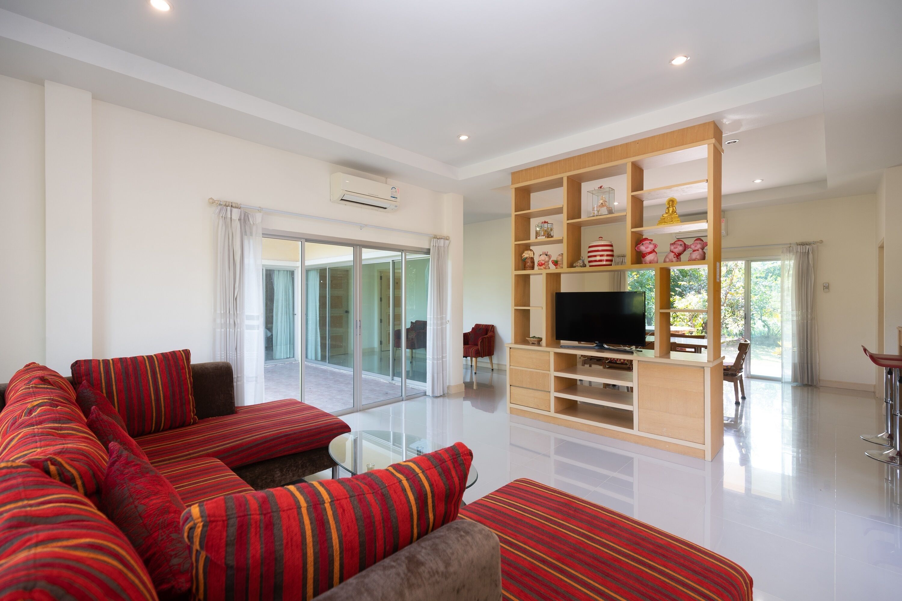 A modern living room with a sectional sofa, a TV on a wooden stand, and a glass door leading to a balcony.