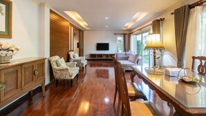 A spacious living room with a wooden floor, a sofa, a TV, and a dining area with a table and chairs. - Thara Cholapruek Resort (Ban Na)
