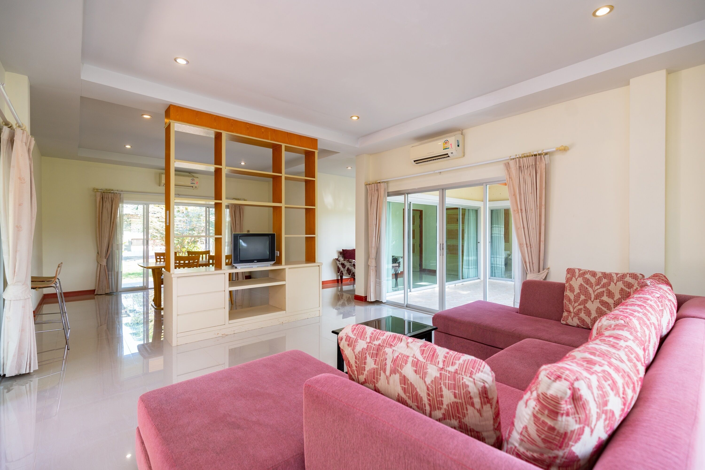 A modern living room with a pink sofa, a TV on a wooden stand, and a glass table.