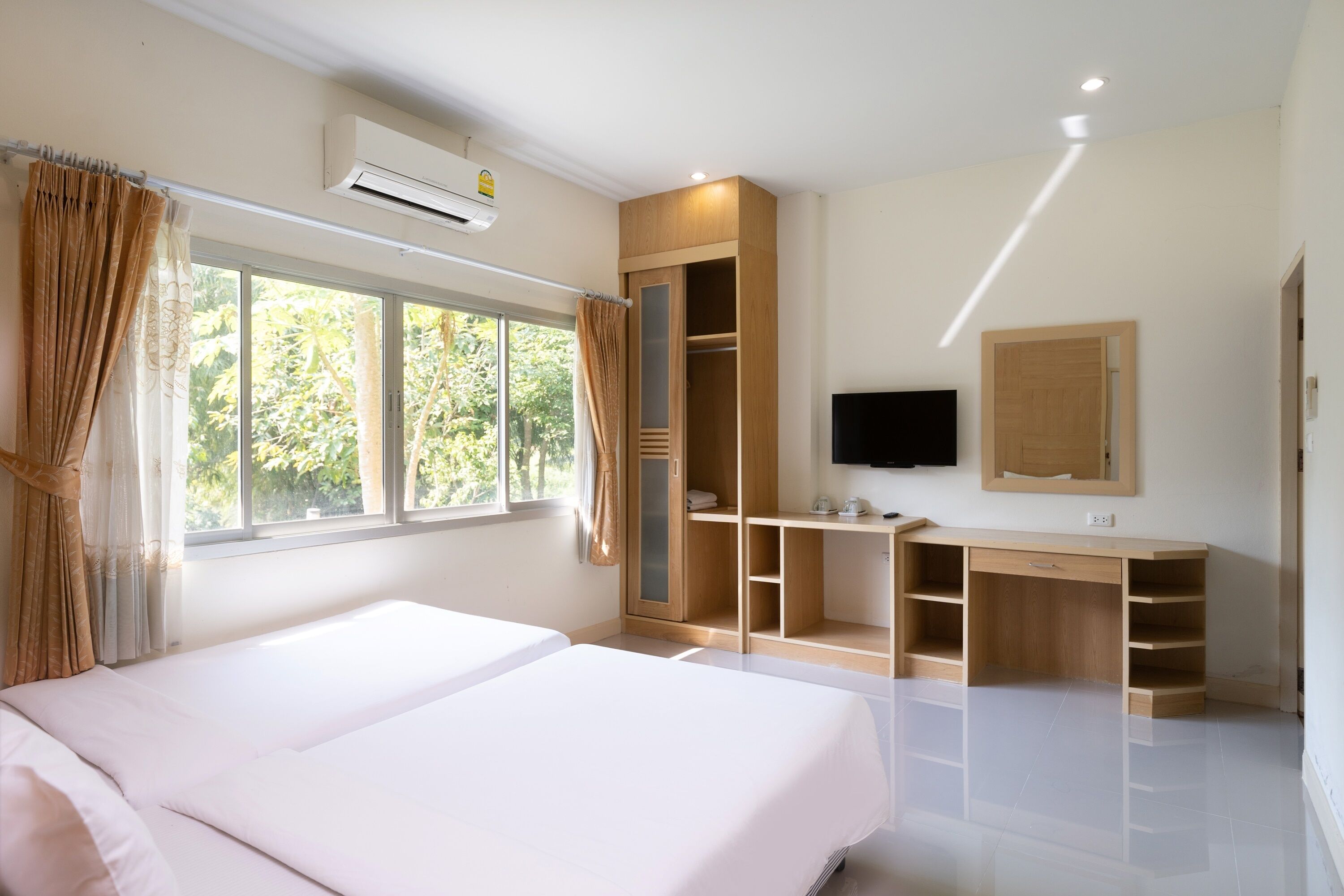 A bedroom with two beds, a desk, a wardrobe, and a TV.