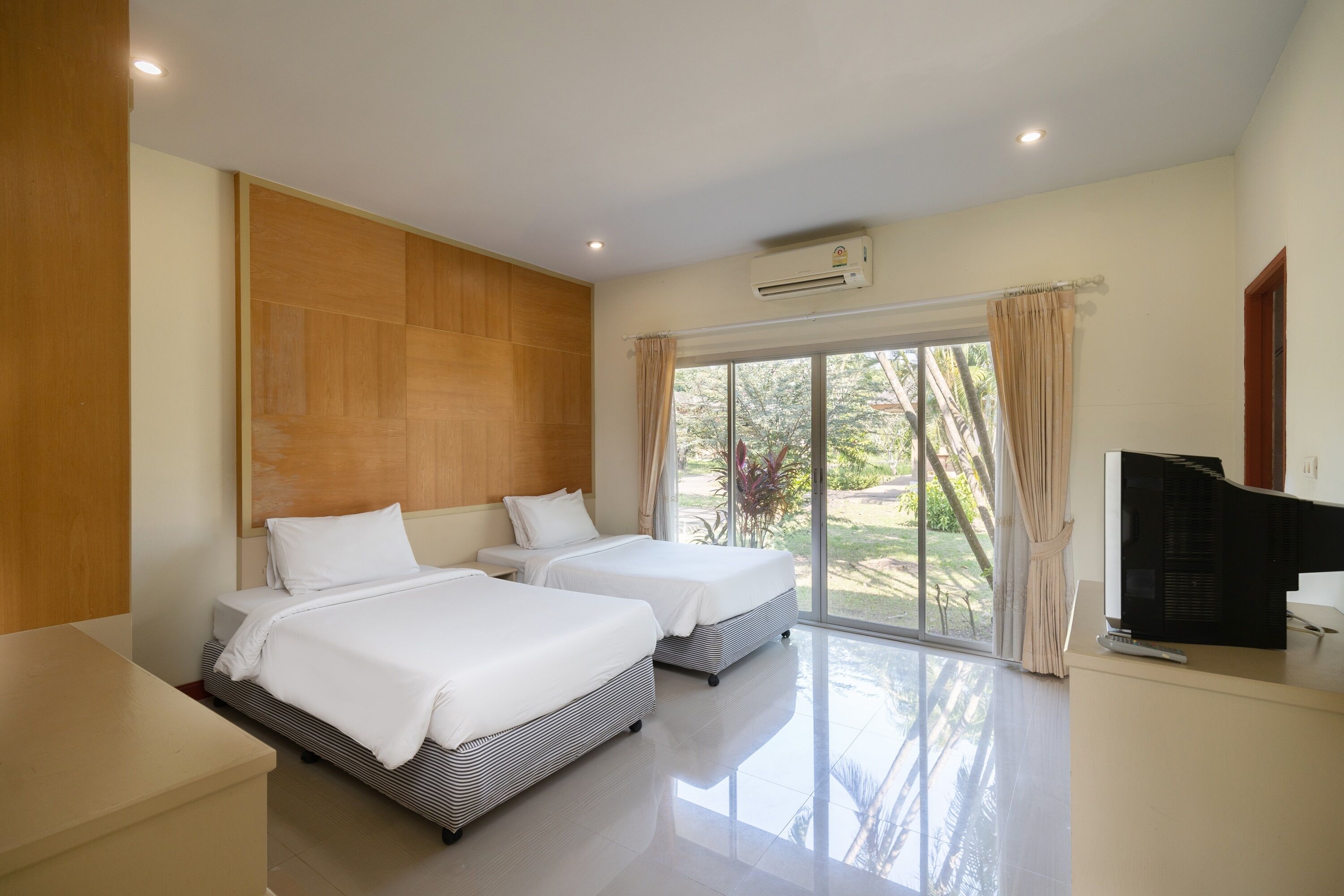 A hotel room with two beds, a TV, and a large window with curtains.
