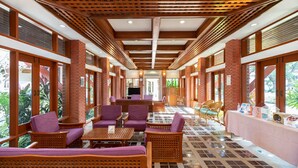 A spacious indoor area with wooden furniture, brick pillars, and large windows allowing natural light. - Thara Cholapruek Resort (Ban Na)