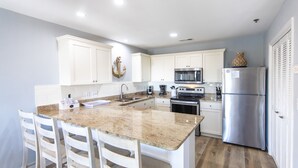 A modern kitchen with white cabinets, a granite countertop, stainless steel appliances, and a bar area with white chairs. - Gulf view, private beach, community pool, walk to shops and restaurants! (Santa Rosa Beach)