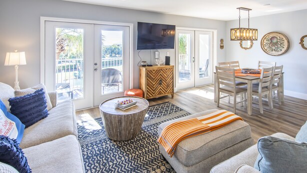 A spacious living room with a ceiling fan, a flat-screen TV, a dining area with wooden chairs, and a large window overlooking a balcony. - Gulf view, private beach, community pool, walk to shops and restaurants! (Santa Rosa Beach)