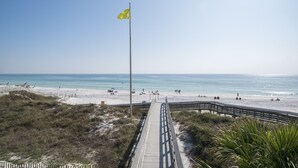 A beach with a wooden boardwalk leading to the shore, a flagpole with a flag, and a clear blue sky. - Gulf view, private beach, community pool, walk to shops and restaurants! (Santa Rosa Beach)