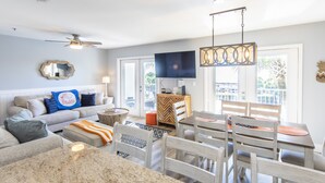 A modern living room with a sofa, coffee table, and dining area with chairs and a TV. - Gulf view, private beach, community pool, walk to shops and restaurants! (Santa Rosa Beach)