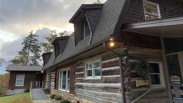 A log cabin with a stone foundation, a front porch, and a signboard. - Far Horizons #416 (Gatlinburg)