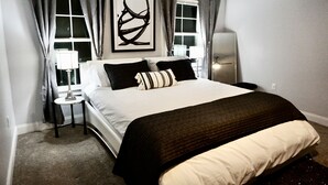 Une chambre à coucher bien rangée, avec un grand lit, une table de chevet, une lampe et une œuvre d’art accrochée au mur.