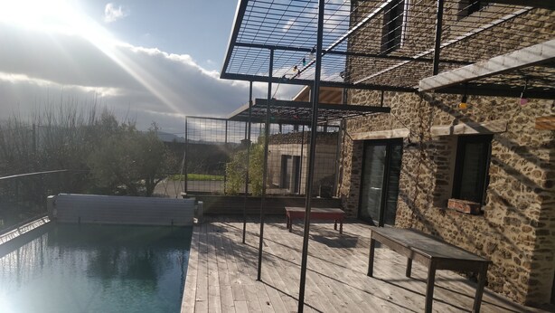 A wooden deck with a swimming pool, stone walls, and a metal pergola. - Charming house with swimming pool (Saint-Chamond)