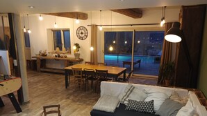 A cozy living room with a sofa, wooden coffee table, and dining area with a table and chairs. There is a large window with a view of a swimming pool and a patio outside. - Charming house with swimming pool (Saint-Chamond)