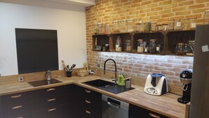 A modern kitchen with a brick wall, built-in shelves with jars, a dishwasher, and a coffee maker. - Charming house with swimming pool (Saint-Chamond)