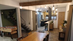 A spacious dining area with a wooden table and chairs, a foosball table, and a kitchen in the background. - Charming house with swimming pool (Saint-Chamond)