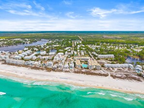 An aerial view of a coastal resort with beachfront properties, a marina, and a large pool area.