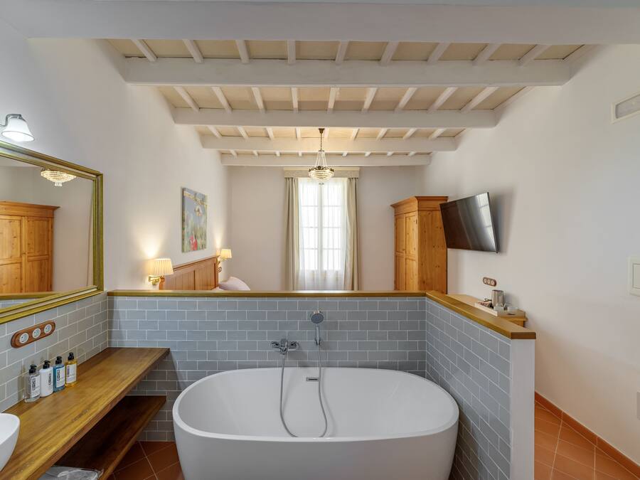 Un baño moderno con una bañera independiente, un tocador de madera, un espejo grande y un televisor montado en la pared.